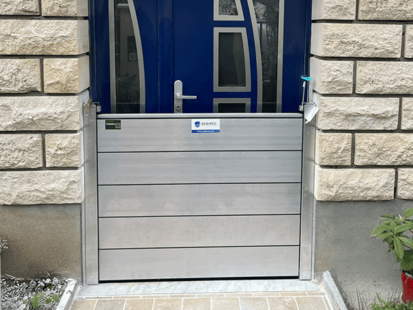 Porte d’entrée bleue d’une maison en pierre avec un batardeau CASTOR+ en place : cinq palplanches aluminium empilées