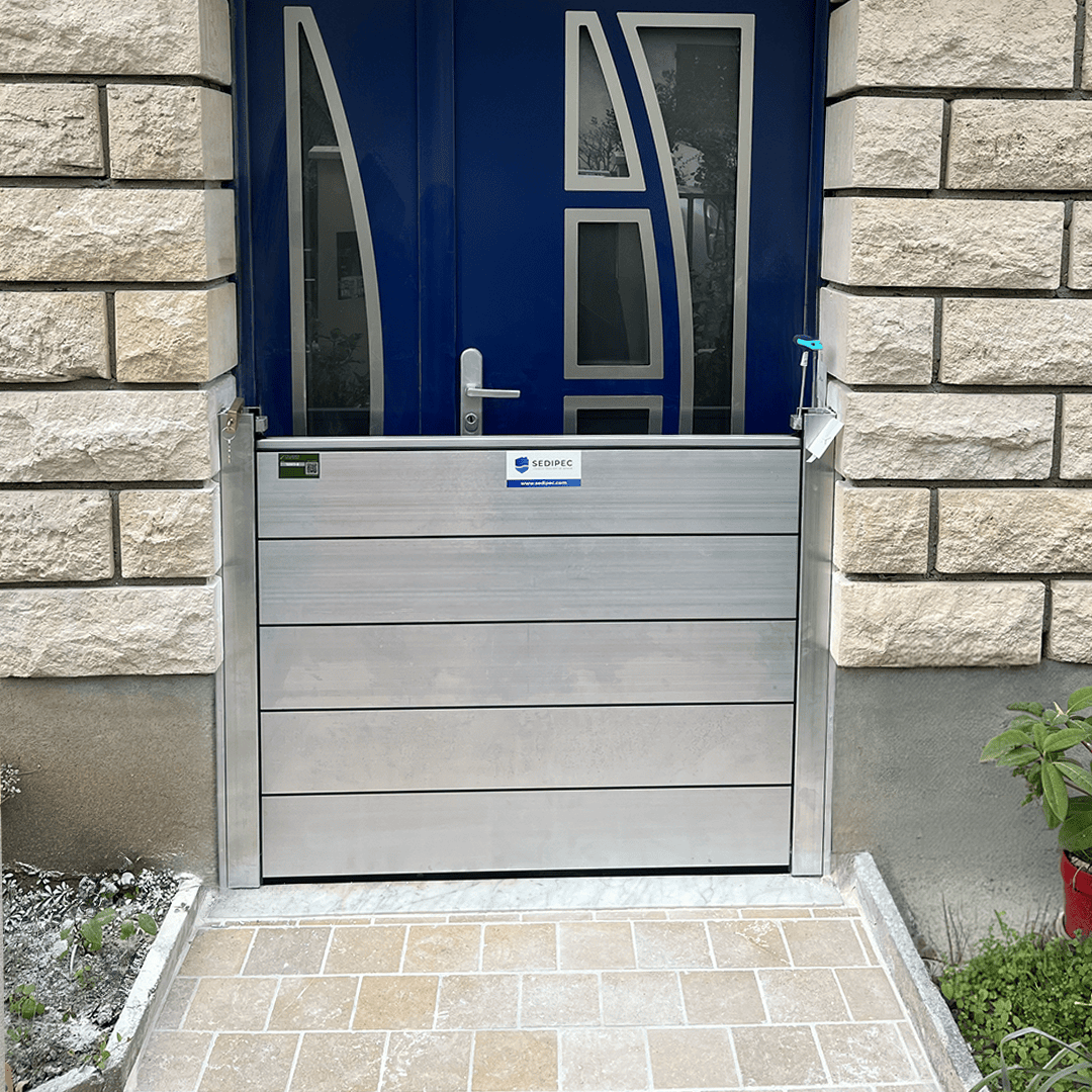 Porte d’entrée bleue d’une maison en pierre avec un batardeau CASTOR+ en place : cinq palplanches aluminium empilées