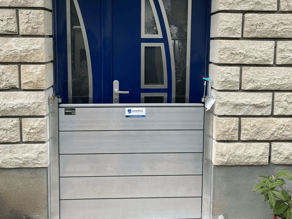 Porte d’entrée bleue d’une maison en pierre avec un batardeau CASTOR+ en place : cinq palplanches aluminium empilées