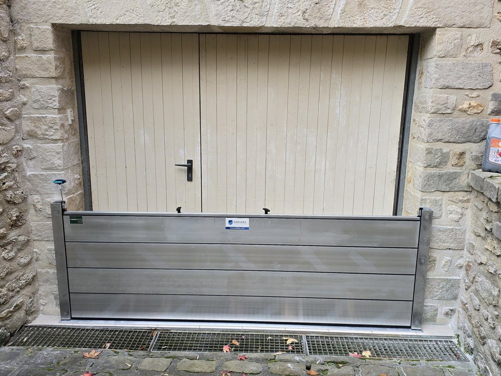 Batardeau amovible en aluminium posé devant une porte de garage, à retirer après la crue
