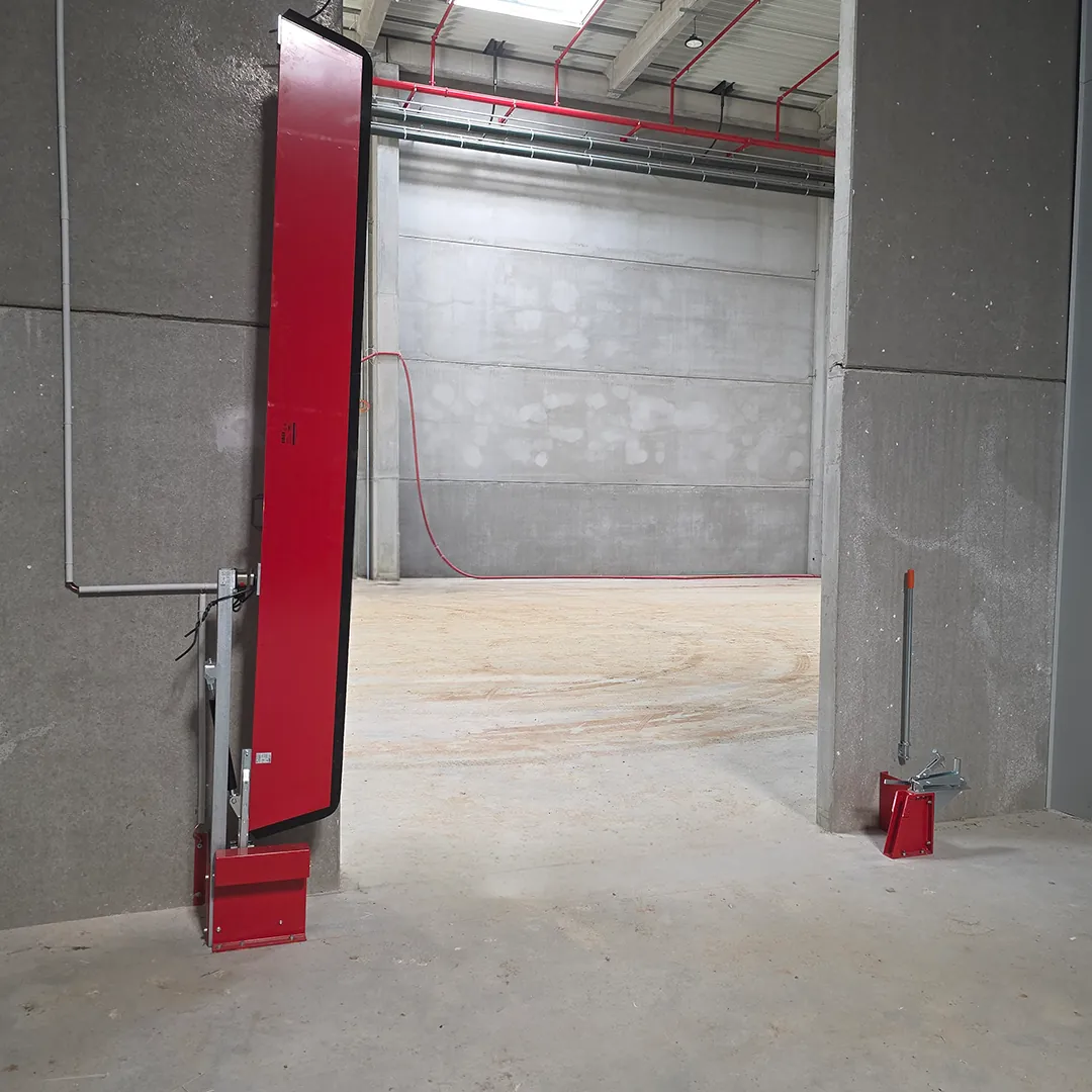 Barrière de rétention automatique rouge en position relevée le long d'une ouverture dans un local en béton