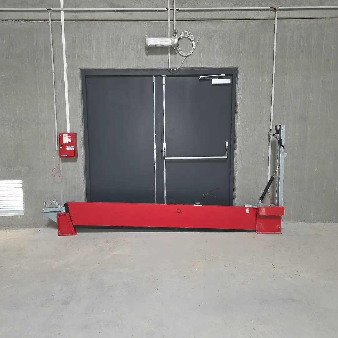 Barrière de rétention rouge abaissée au pied d'une porte double dans un local en béton