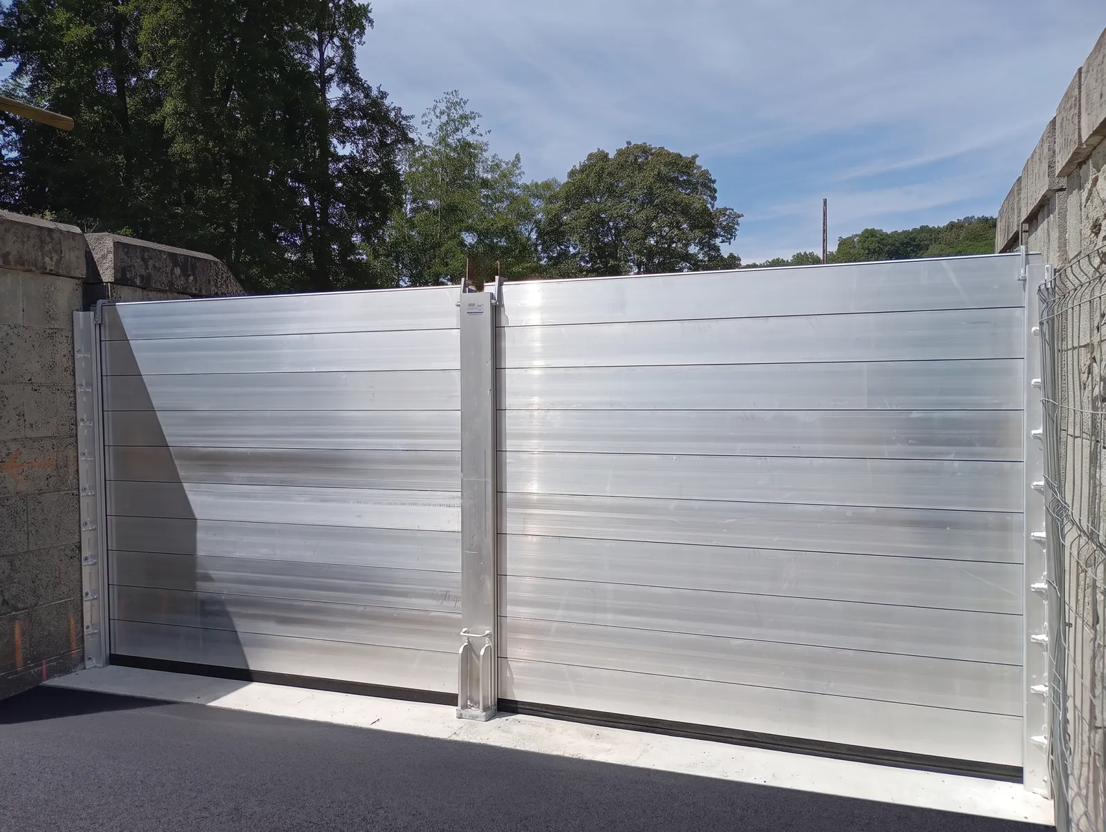 Batardeau anti-inondation en aluminium à lames, en deux travées séparées par un poteau central, fermant une voie entre deux murs de pierre à Montlouis-sur-Loire