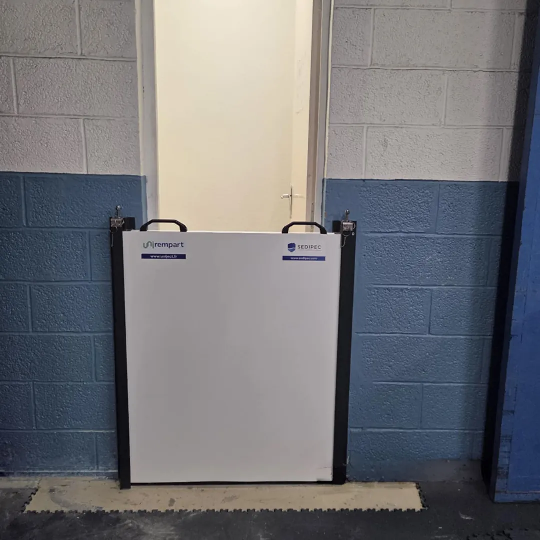 Batardeau monobloc à poignées devant une porte simple dans un couloir d'entrepôt