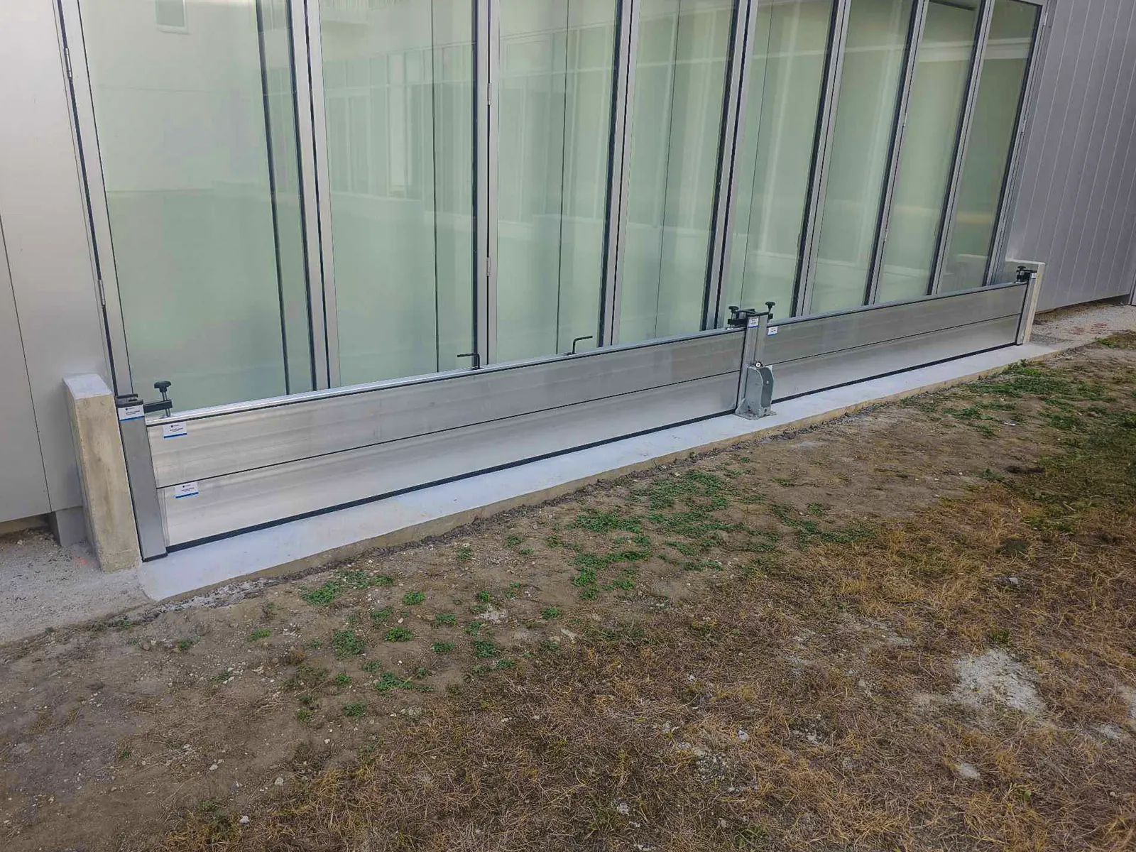 Deux travées de batardeaux aluminium et leur poteau central au pied de vitrages