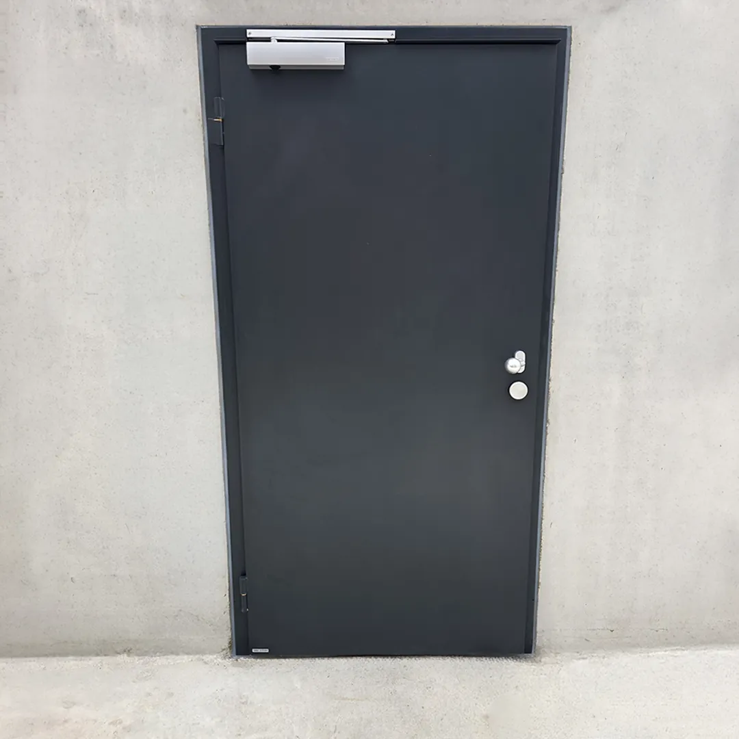 Porte anti-inondation pleine de couleur anthracite avec ferme-porte, posée dans un mur en béton