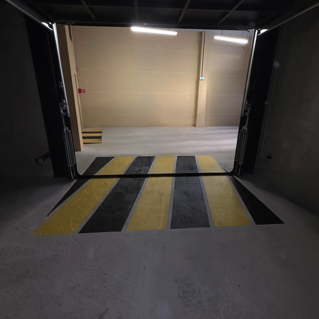 Accès de parking souterrain ouvert, porte relevée et marquage jaune et noir au sol