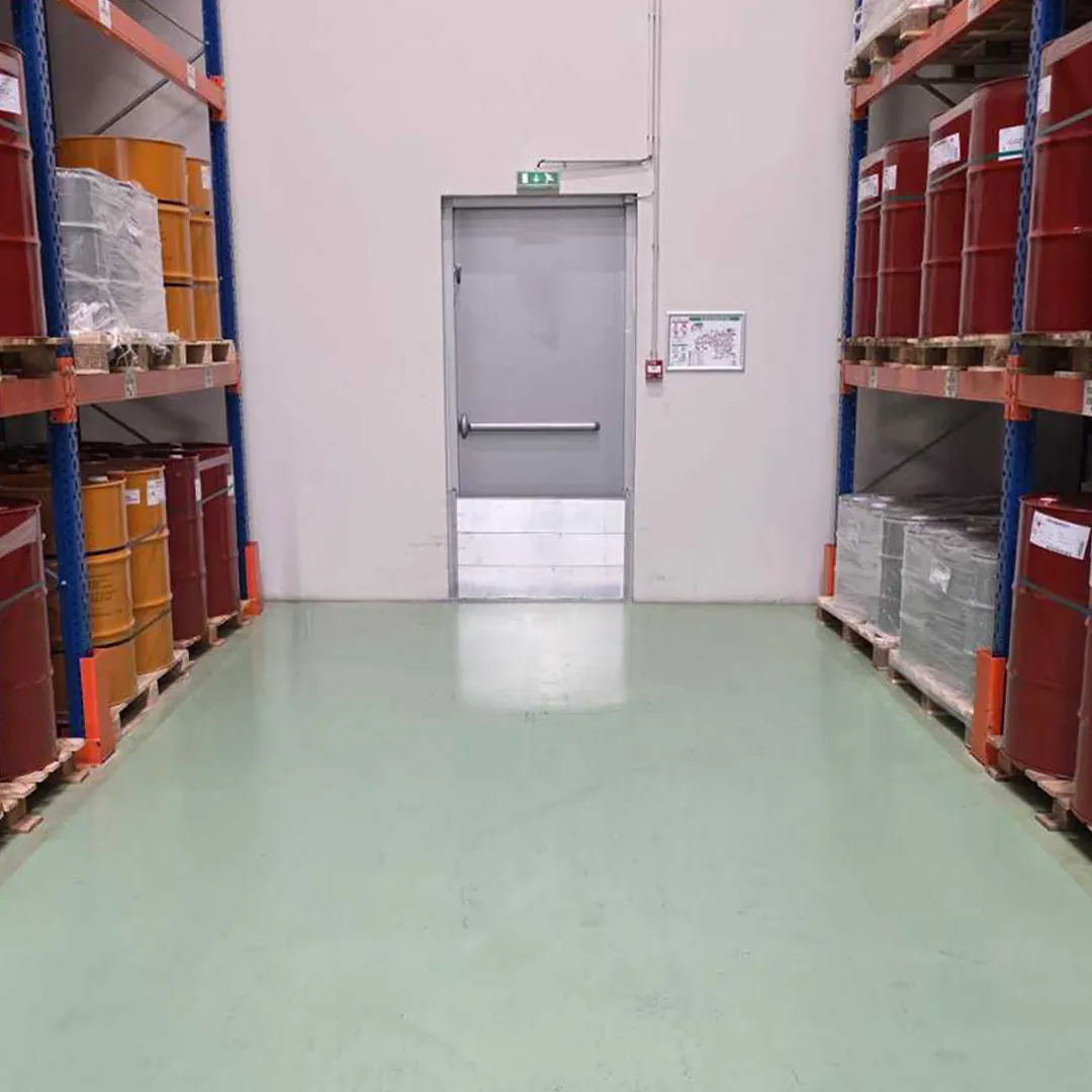 Seuil de rétention des eaux d'extinction au bas d'une porte d'issue, dans une allée de stockage de fûts sur racks