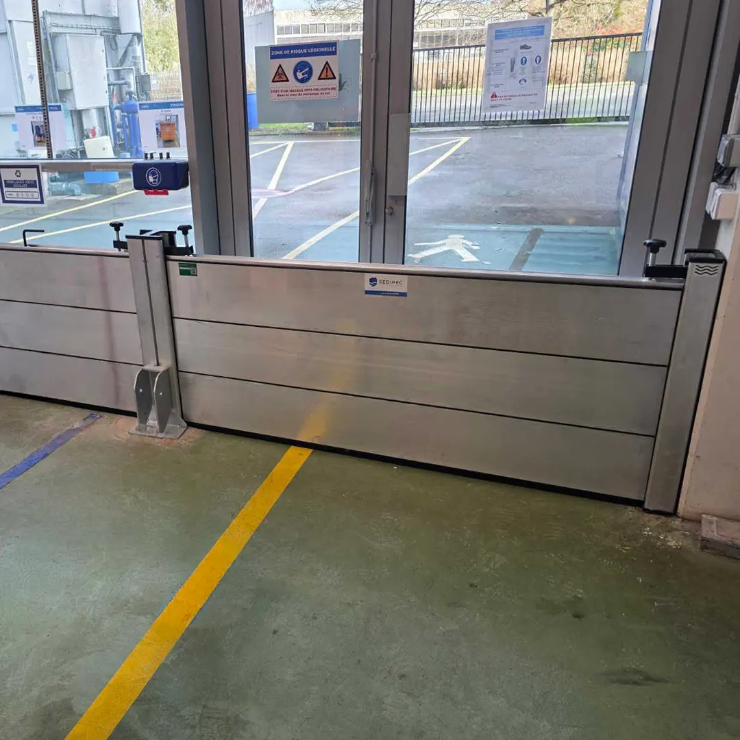 Batardeau aluminium à lames avec poteau intermédiaire, posé devant une porte vitrée de laboratoire