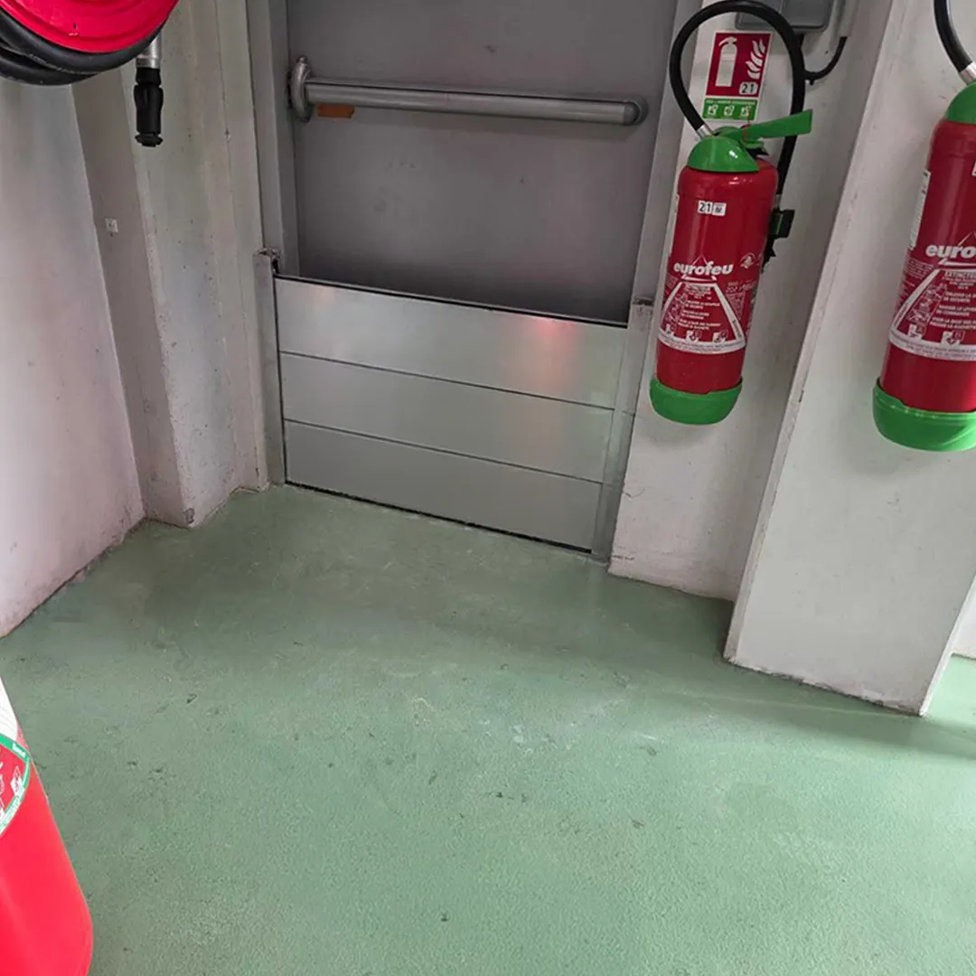 Batardeau aluminium au bas d'une porte d'issue, à côté d'extincteurs