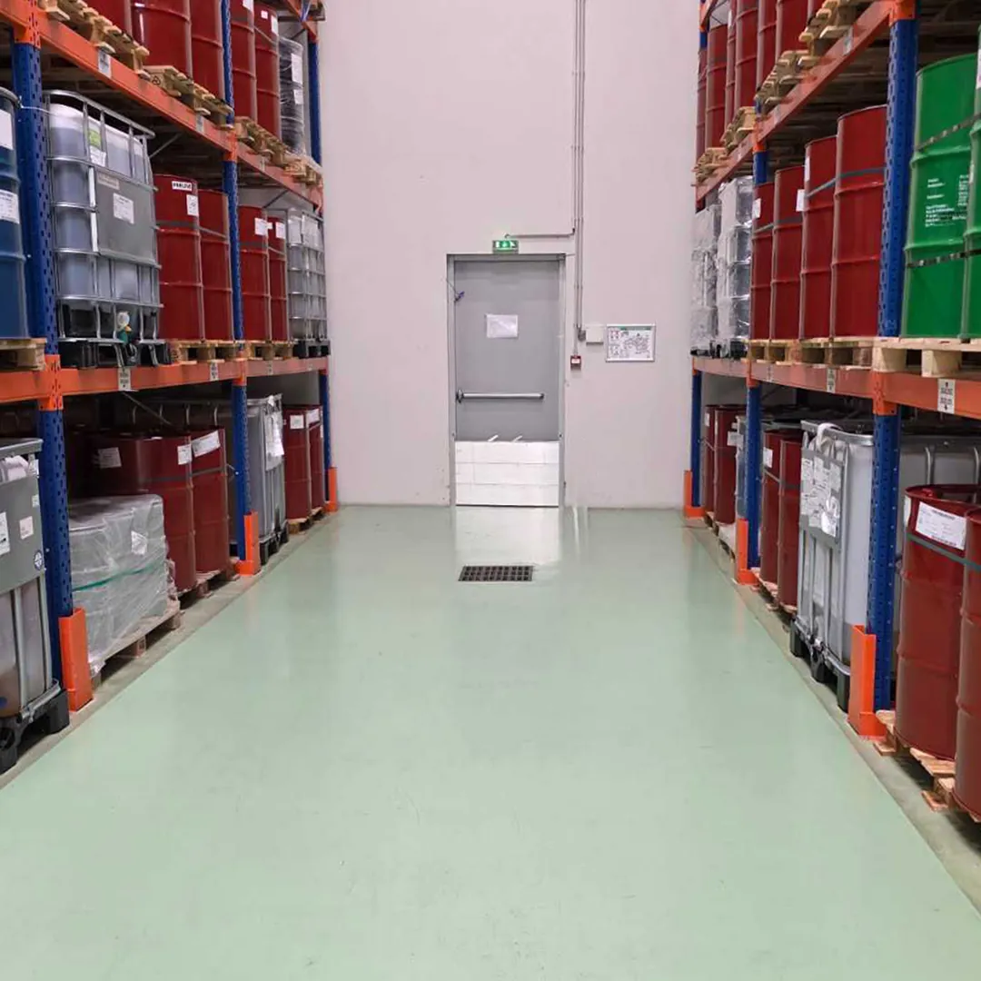 Allée de stockage de fûts sur racks menant à une porte d'issue équipée d'un seuil de rétention